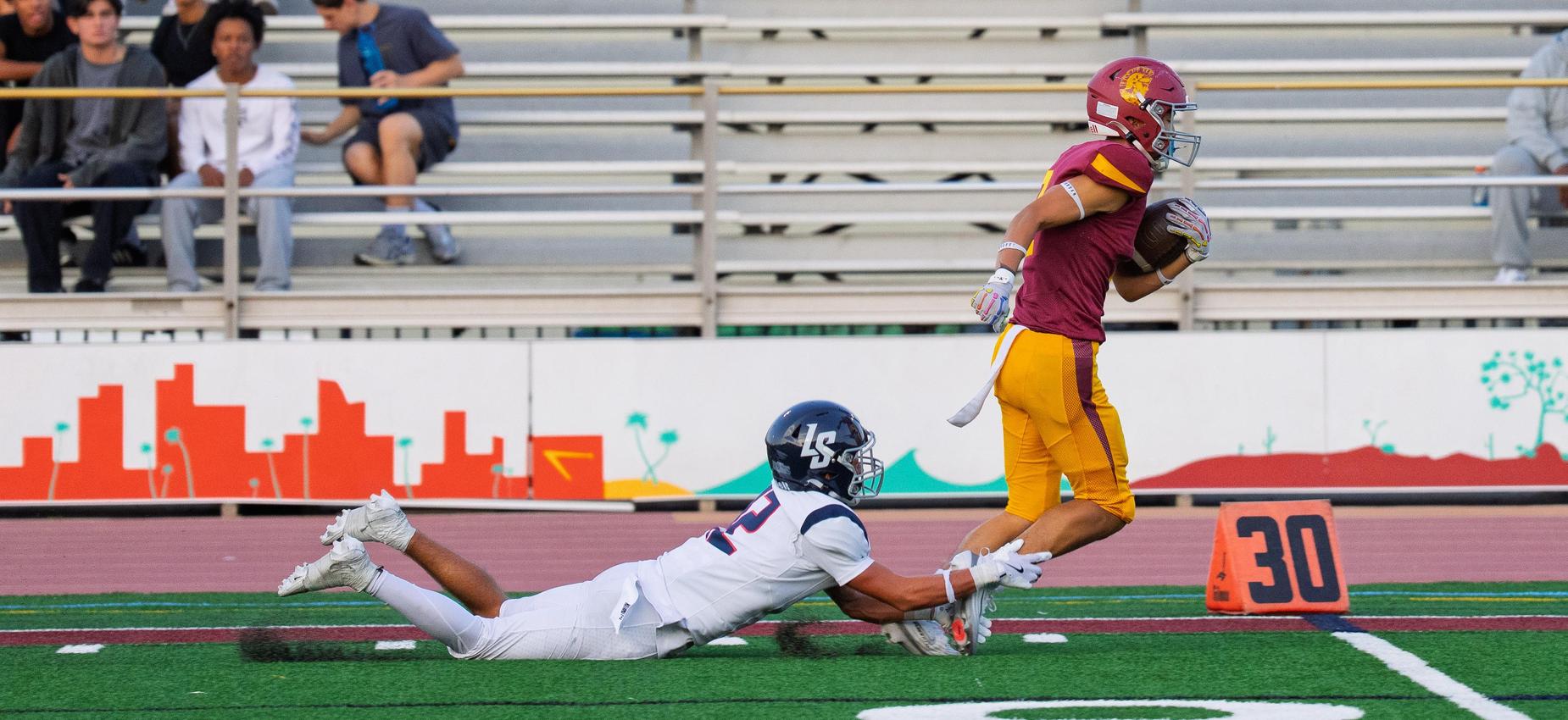 Defensive football player grabbing ankles of offensive player near sideline.