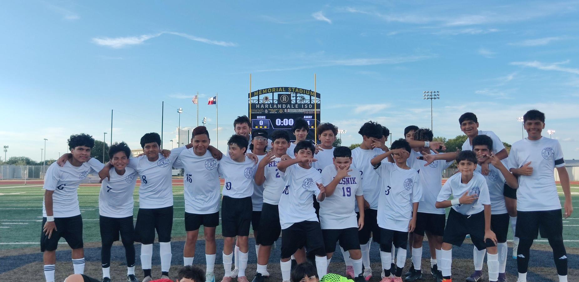 Group of boys in white jerseys celebrating on a sports field.