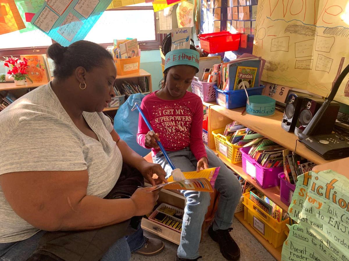 Adult and child engaged in a reading activity in a colorful classroom.