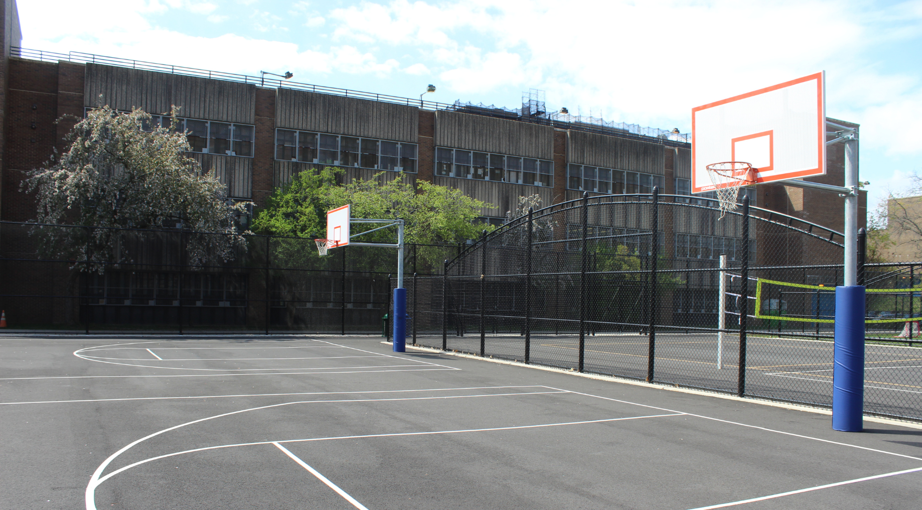 Outdoor basketball court with two hoops and a fenced area.