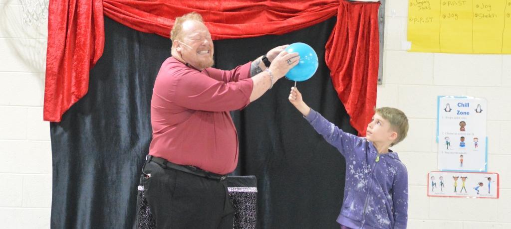 magician and boy perform a trick with a blue balloon