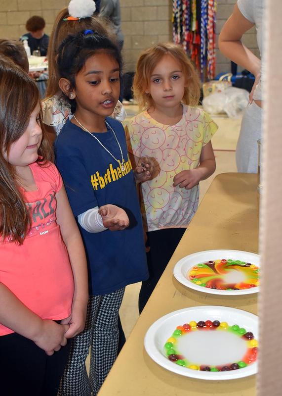 three girls standing next to a science experiment using Skittles and water