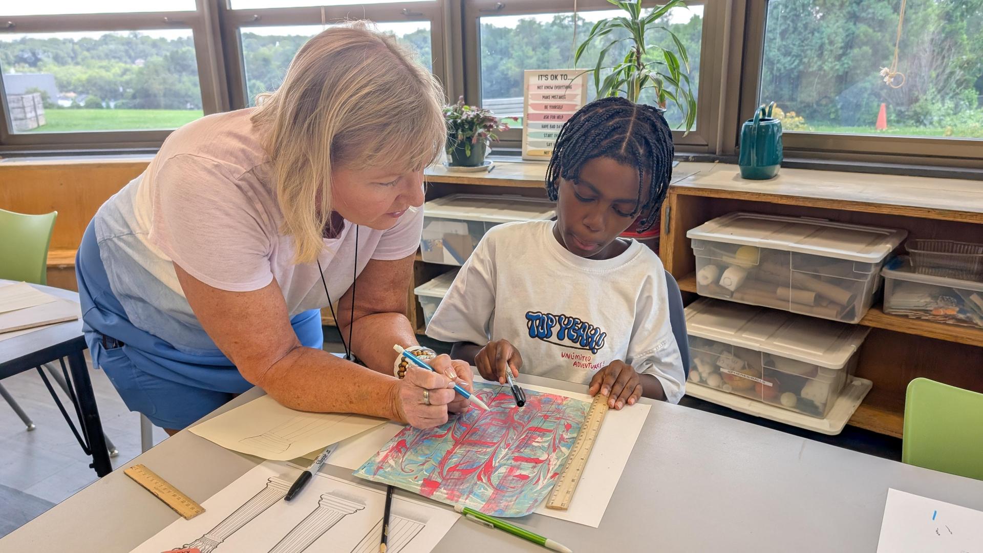 Art teacher working closely with a student 1-1 during art class mastering his brush strokes.