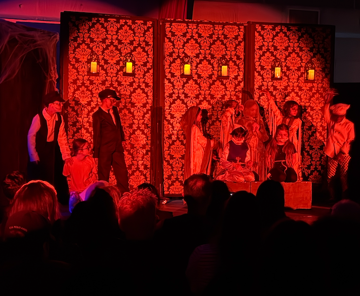 Mummies try to pass on a curse, in a room with red lights and a paisley backdrop.