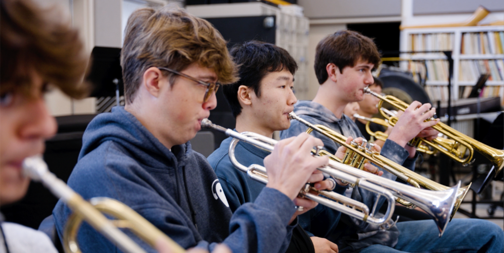 Teenagers playing trumpets in a music class, showcasing collaboration and practice.