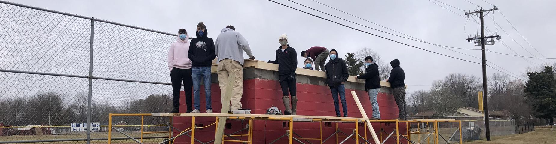 Mr. Hutchins shop class working on putting a new roof on the softball dugouts.