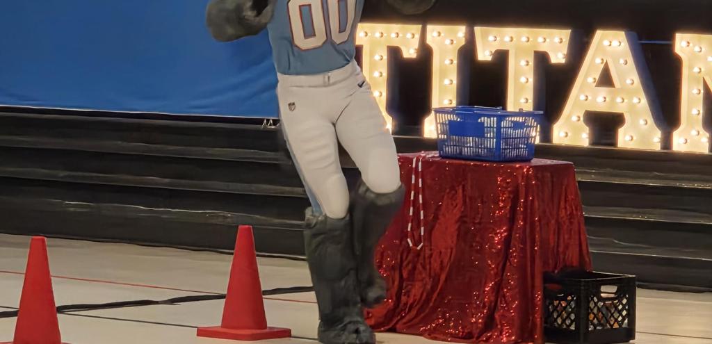 A sports mascot performing near a table with decorations and cones.