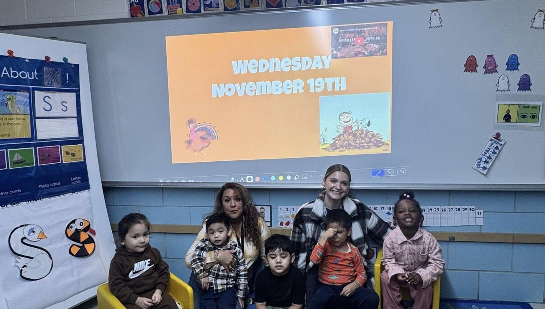Class of children and teachers in a classroom with a colorful bulletin board