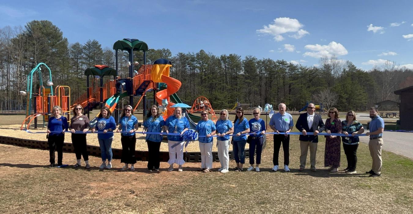 A ribbon-cutting event with a group of people in front of a colorful playground.