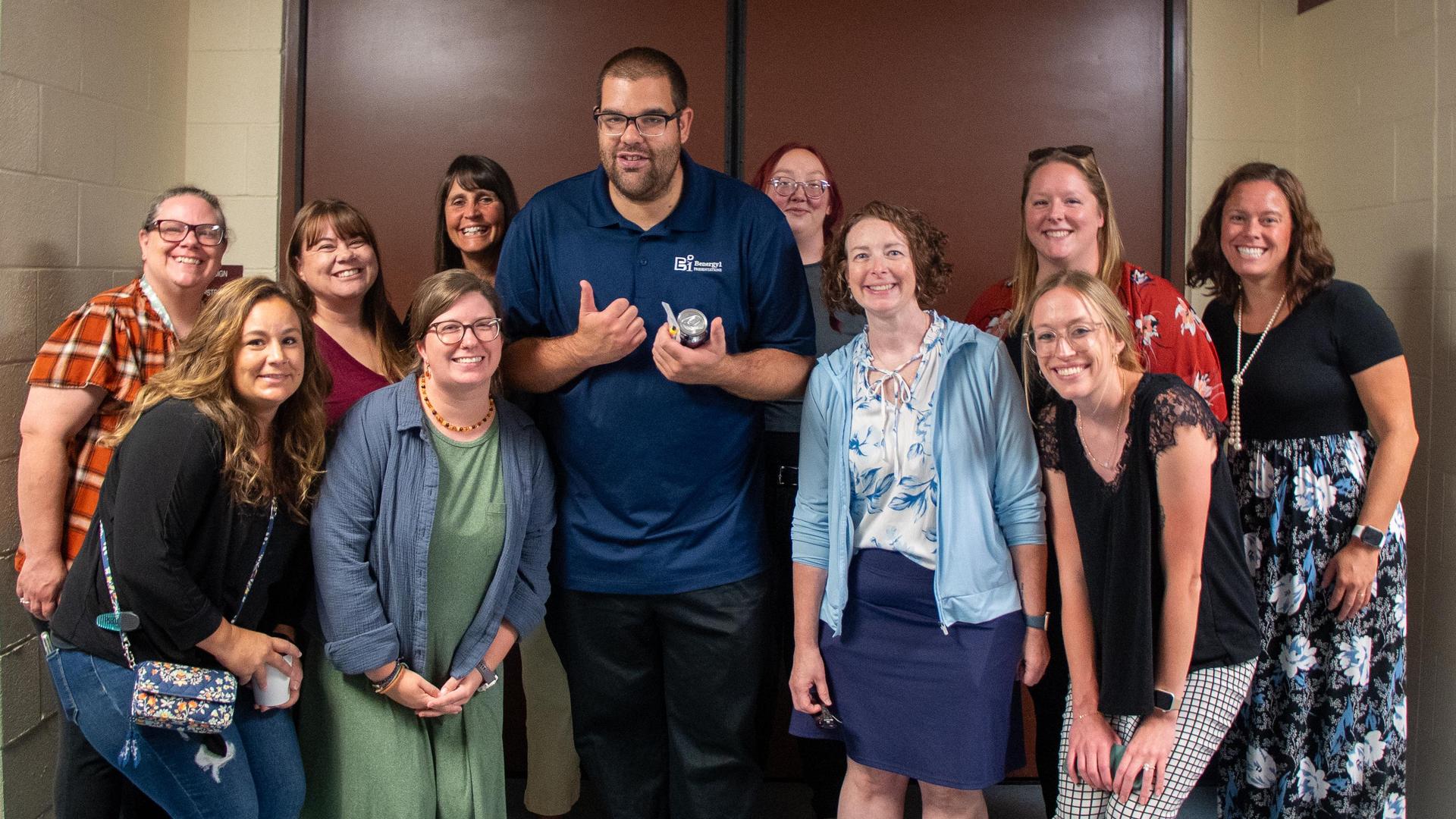 A large group of IU5 staff smiling and posing in a hallway with autism advocate and keynote speaker Ben Hartranft, at an in-service.