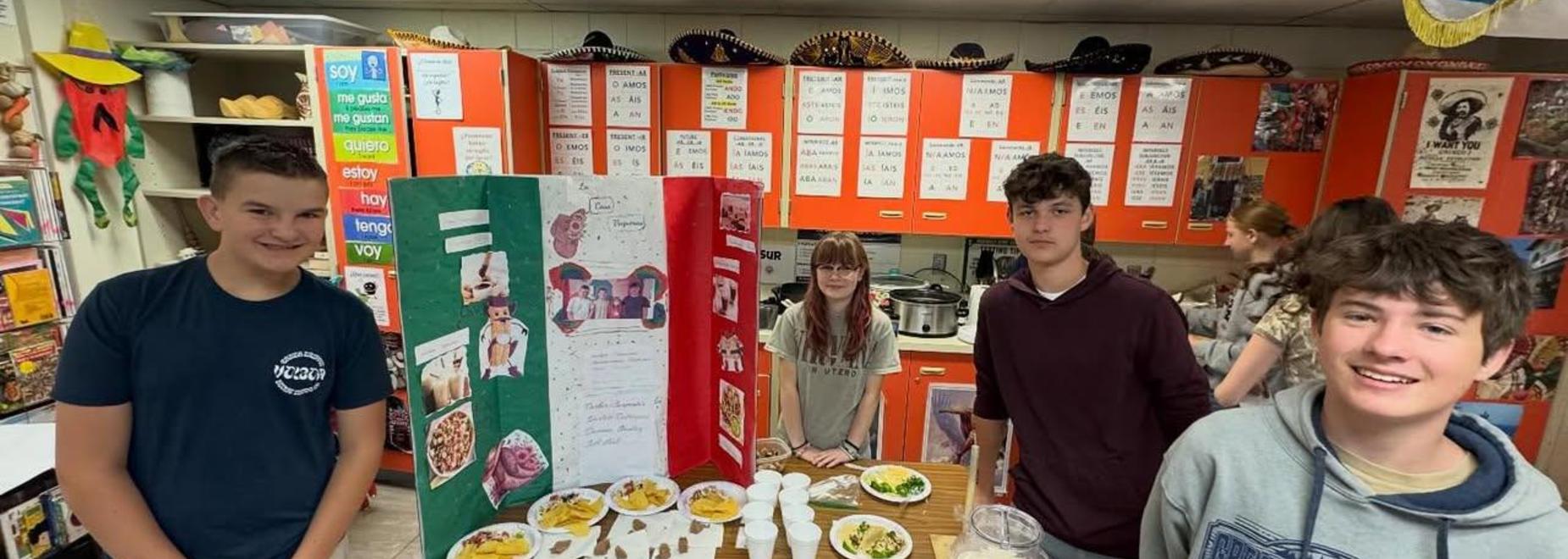 Four students gathered around a display of food and projects celebrating culture.