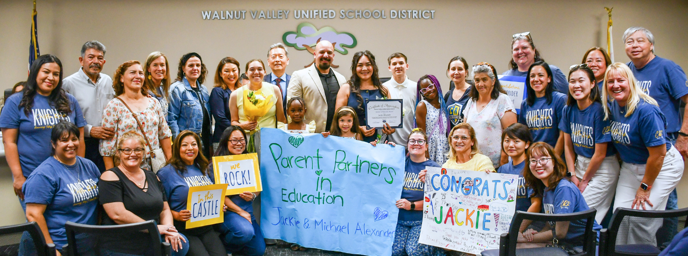 Group celebration with parents and educators, holding signs and awards.