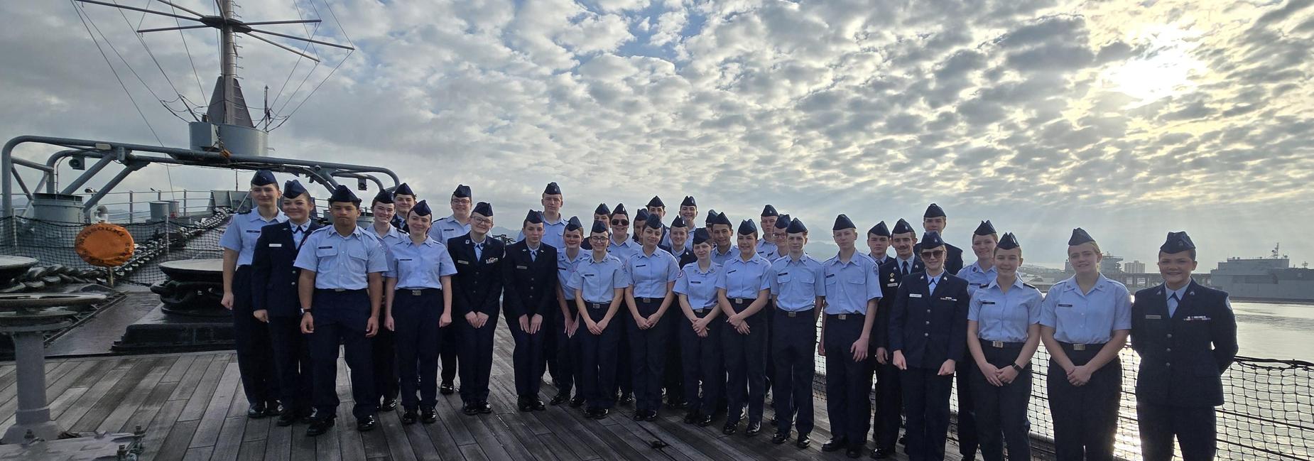 A large group of uniformed individuals on a ship's deck under a cloudy sky.