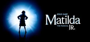 Matilda, the character from the musical, is standing in a spotlight on a stage.