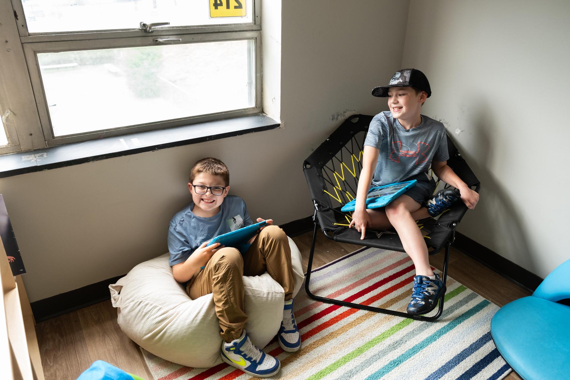 Two boys in classroom with their AAC devices.