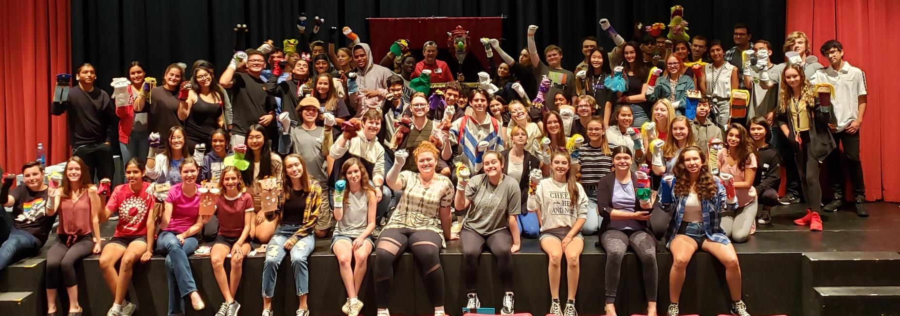 Students on a stage holding sock puppets.