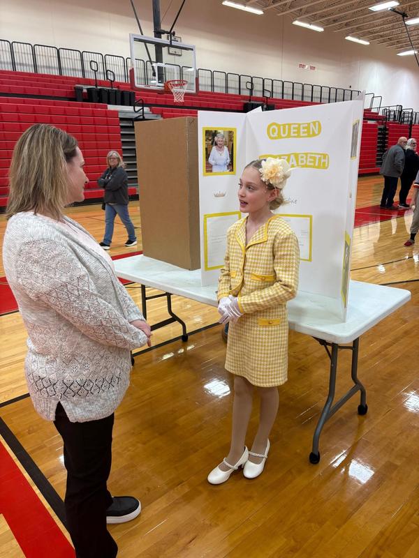 Girl in a yellow dress presenting a project about Queen Elizabeth.
