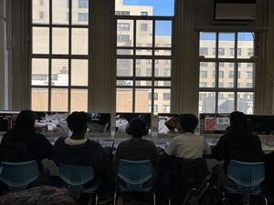 View of multiple students gaming at computers with large windows behind them.