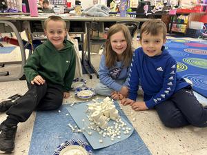 two boys and a girl sitting on floor with a mat full of marshmallows