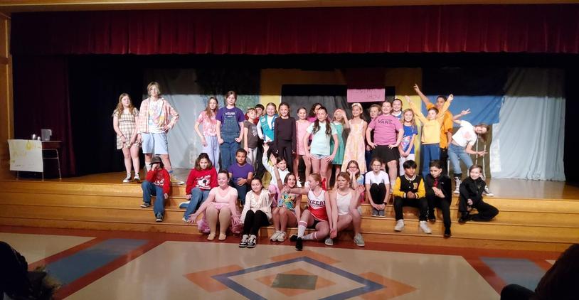 A diverse group of students performing on stage with various props.
