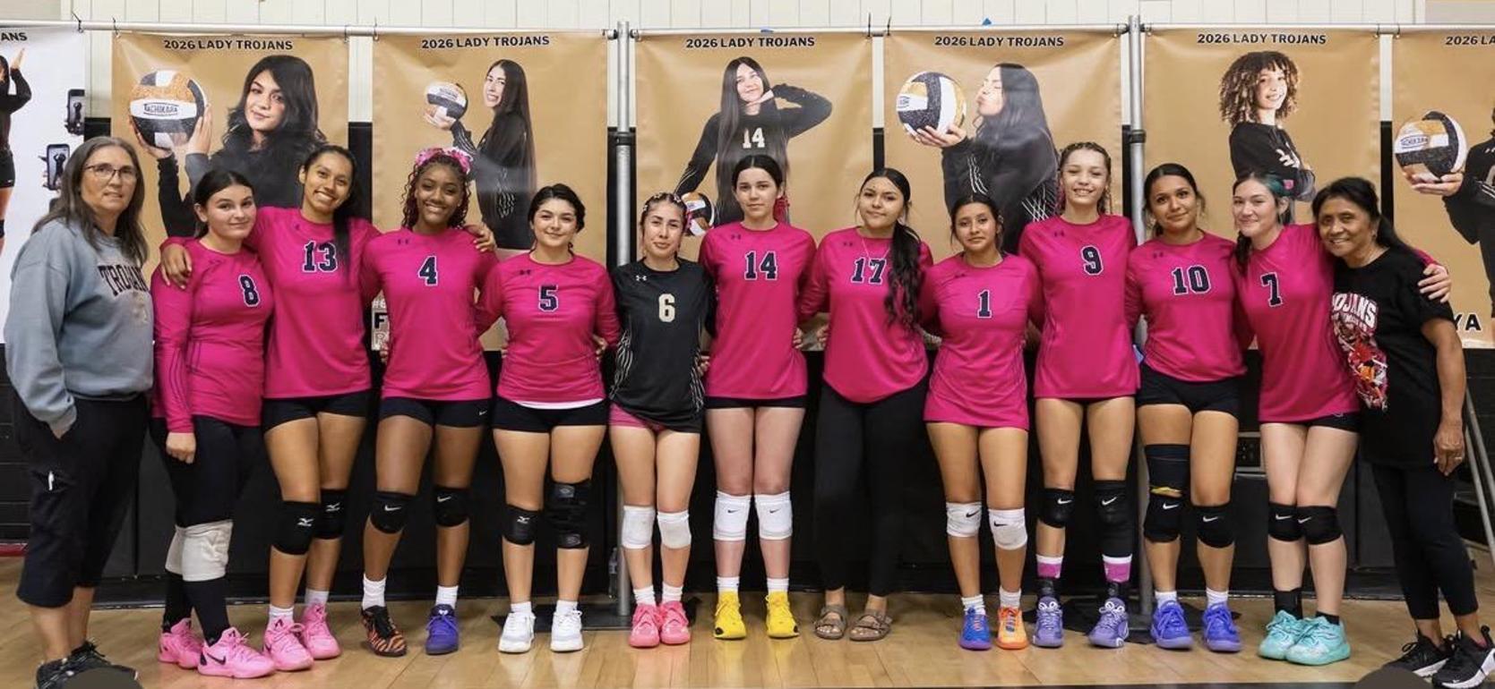 Volleyball team in pink uniforms posing together indoors.