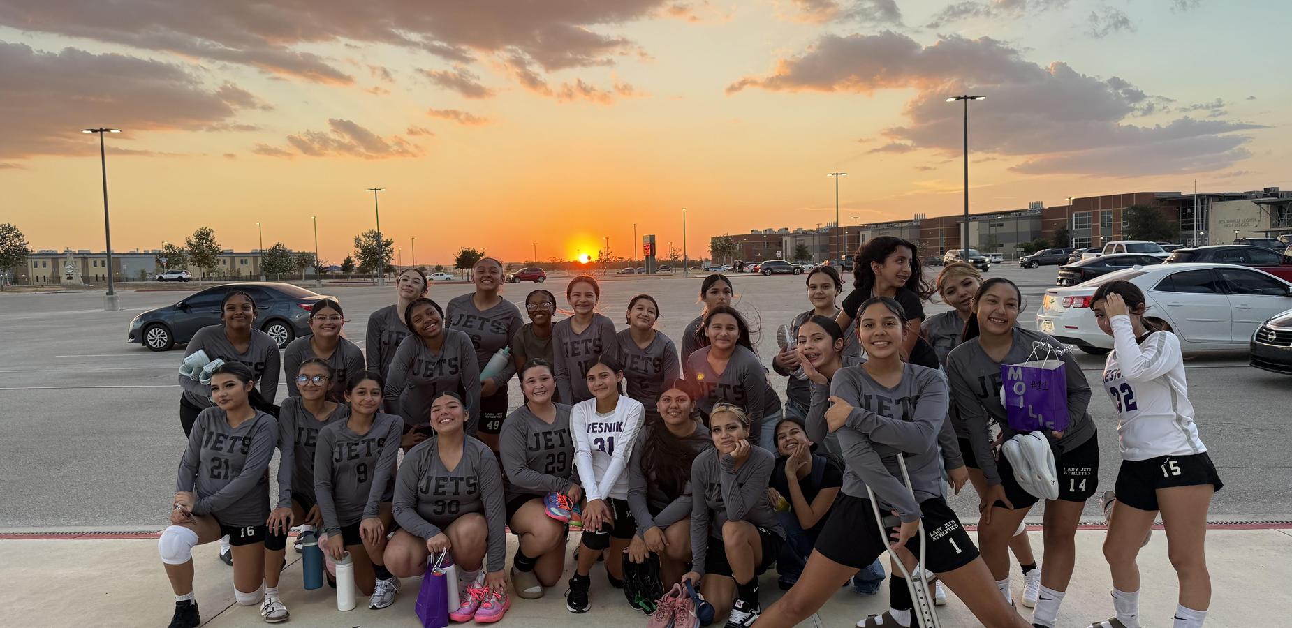 A group of volleyball players in jerseys poses at sunset.