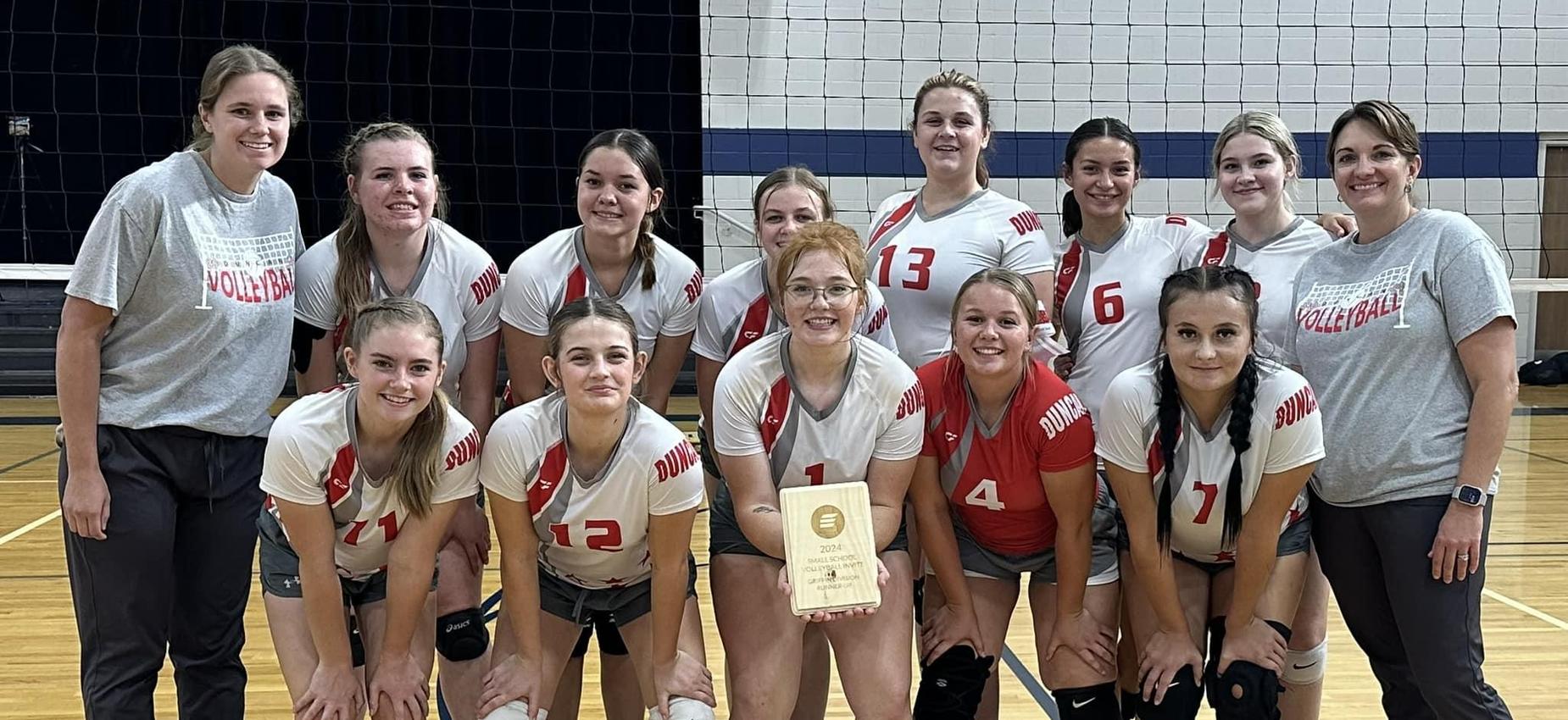 Team of volleyball players celebrating with a trophy in a gym setting.
