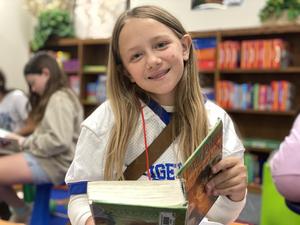 girl elementary student reading book smiling