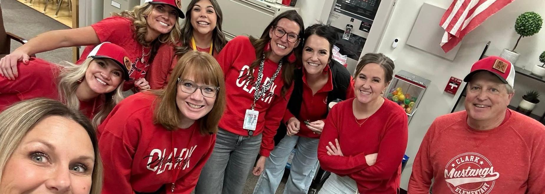 Group of teachers smiling in matching red attire, standing together for a selfie.