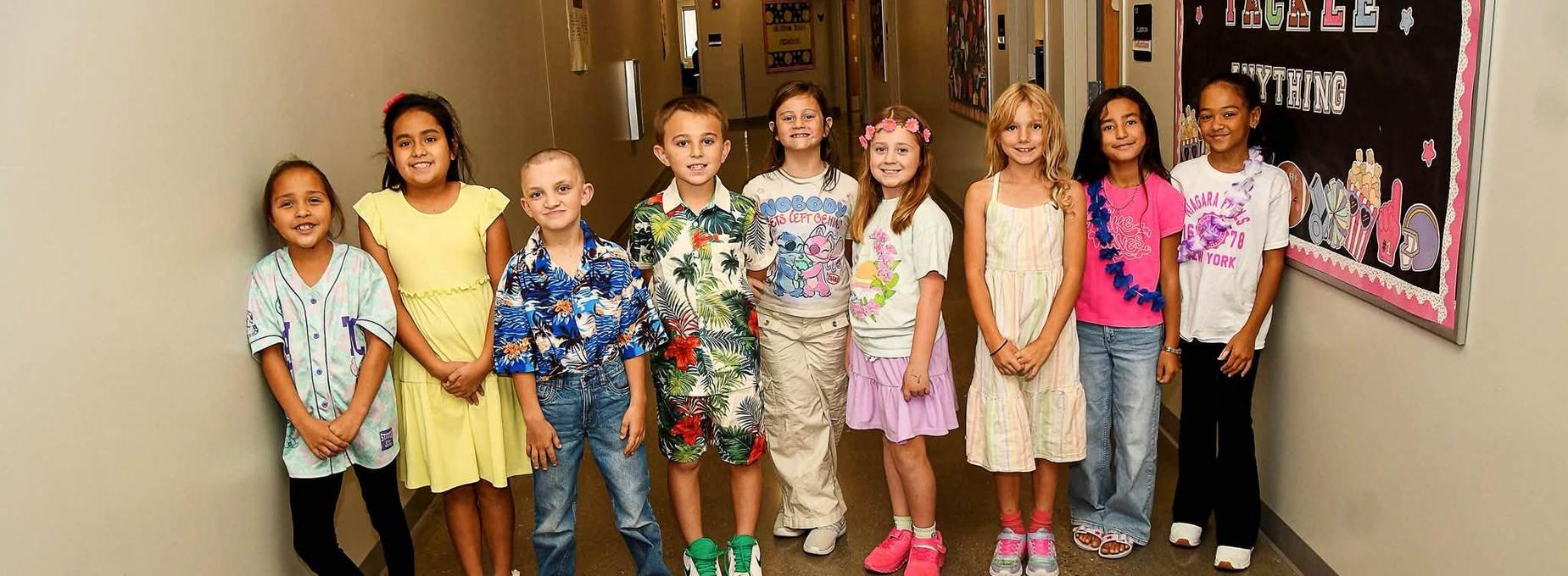 Group of children dressed in colorful outfits standing in a school hallway.