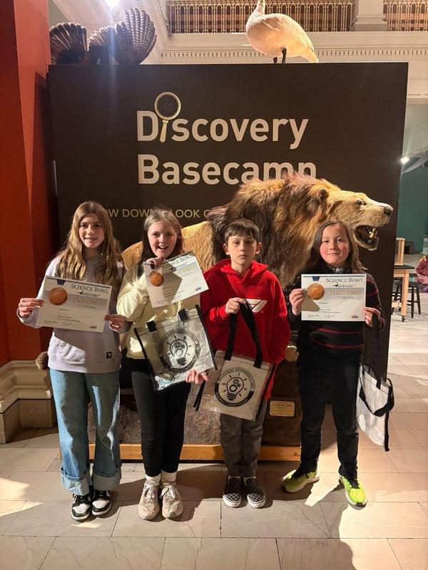 A team of four students holding up their third place certificates at the museum.