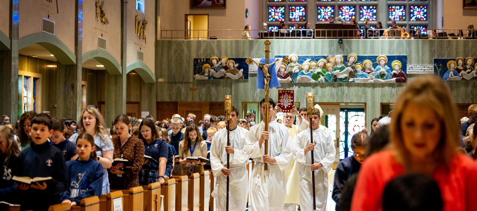 A procession of children in white robes and a colorful mural in a church setting.