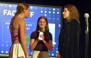 Three girls engaging in a quiz show format with a microphone.