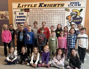 large group of students in rows smiling in front of knight board