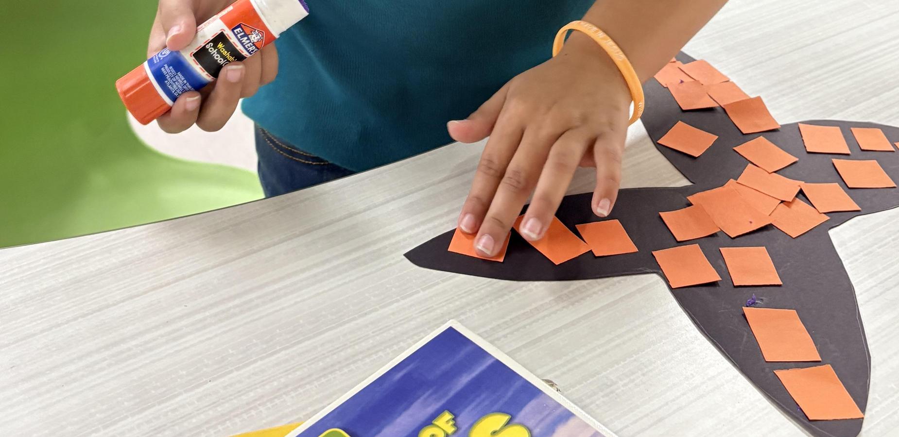 A close-up of a child holding a glue stick while working on a project.
