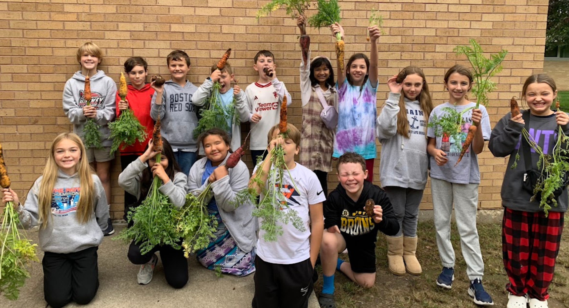 A group of children proudly display freshly harvested carrots outdoors.