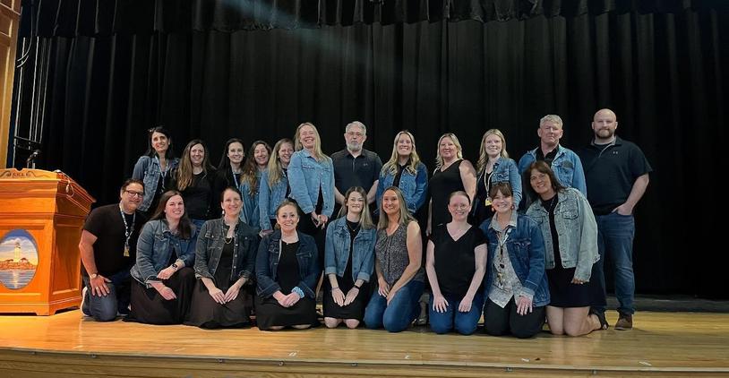 Group of teachers and staff posing on stage with a wooden podium in the background.