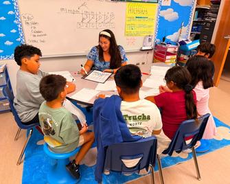 A teacher instructing a group of students sitting around a table.