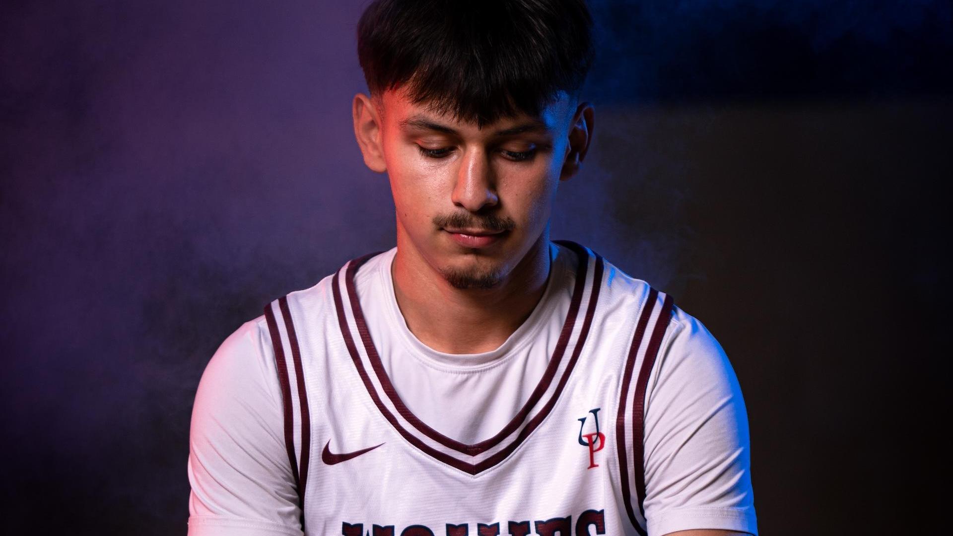 A young man in a basketball jersey holding a ball with colored lighting.