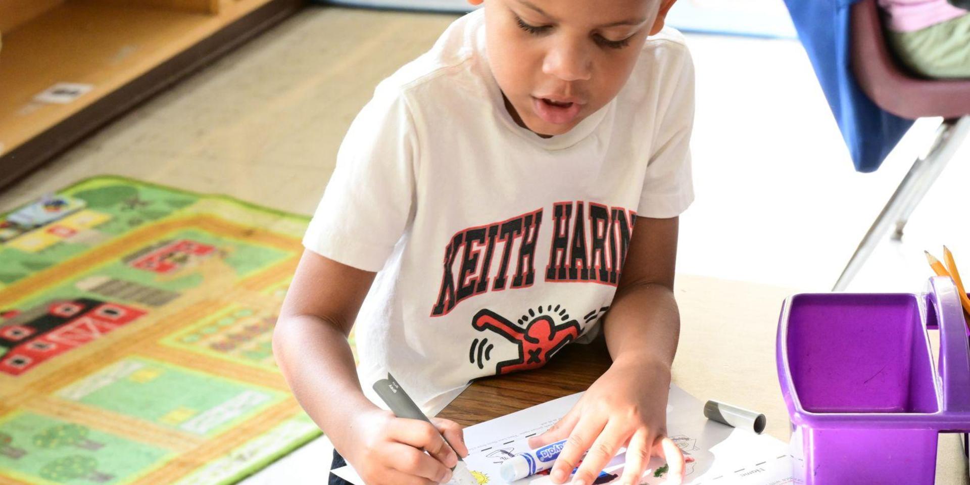 A boy coloring intently on a worksheet at a desk.