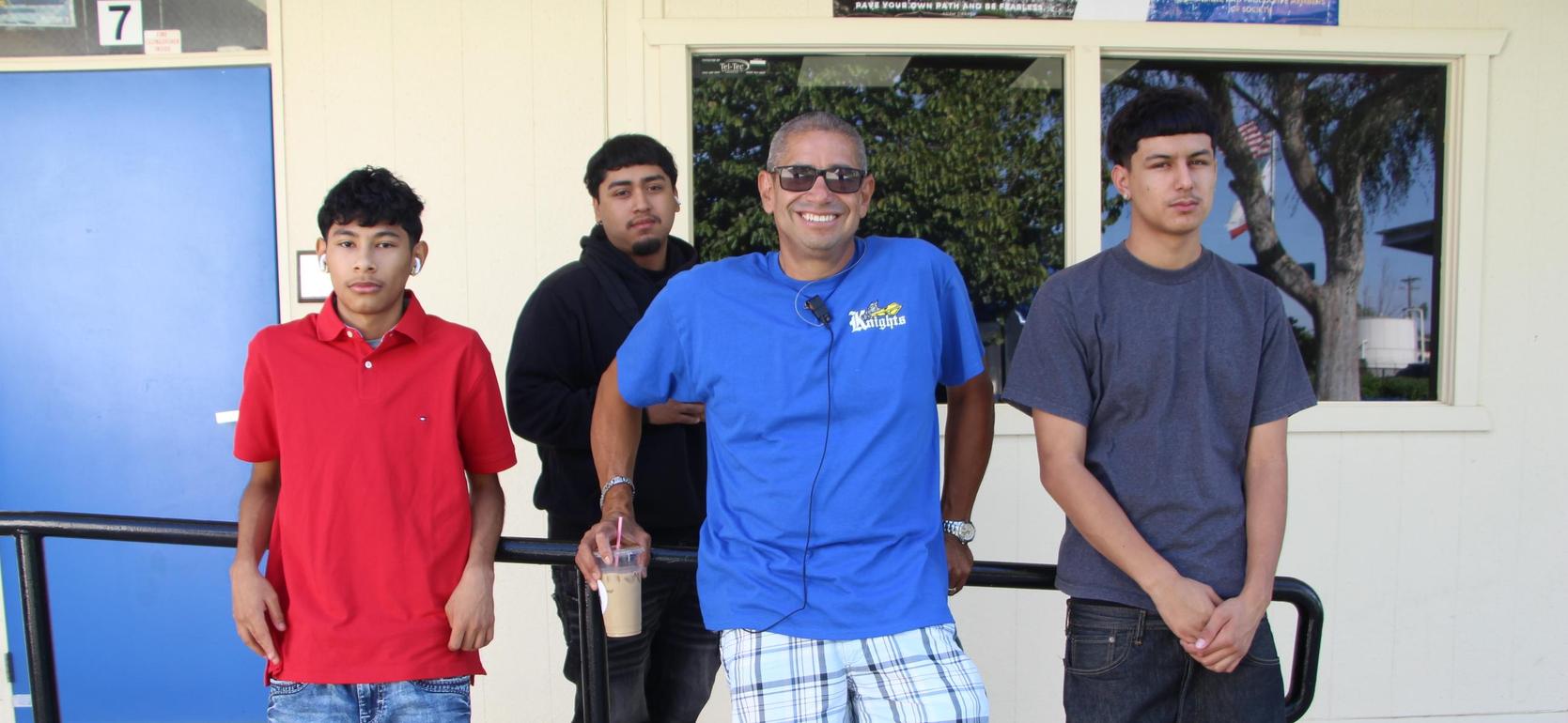 Four men standing outside a building, smiling and posing together.