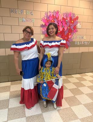Two women in traditional dresses with a child in colorful attire, all smiling.