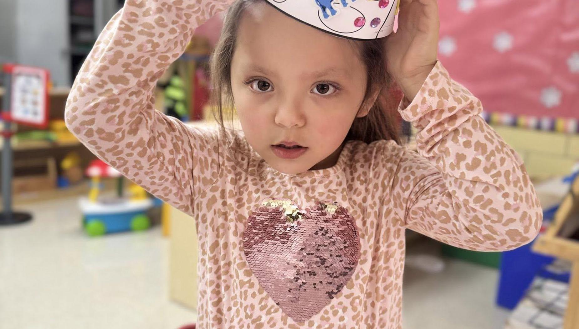 Girl in a leopard print shirt adjusts her decorated hat, looking serious in a playful environment.