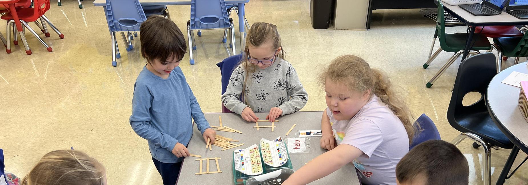 Five students building with popsicle sticks