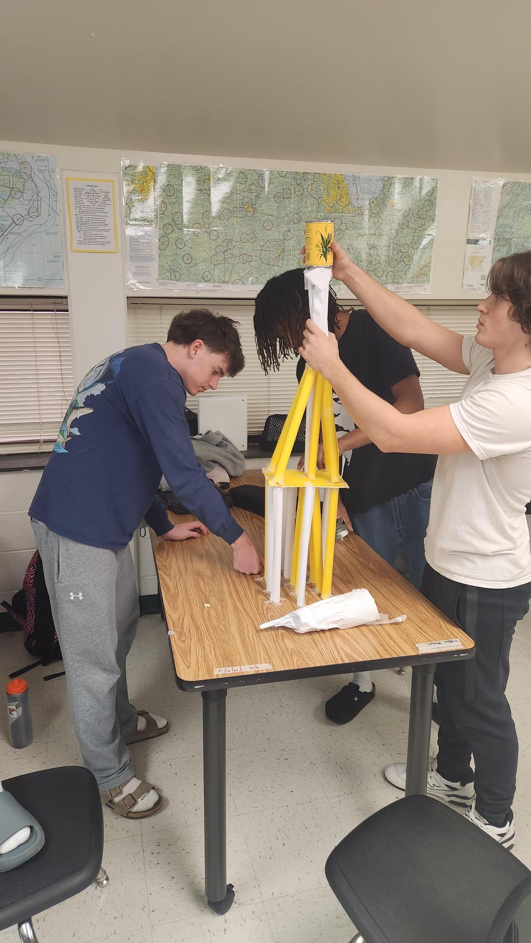 Two students assembling a yellow and white tower at a table in a classroom.