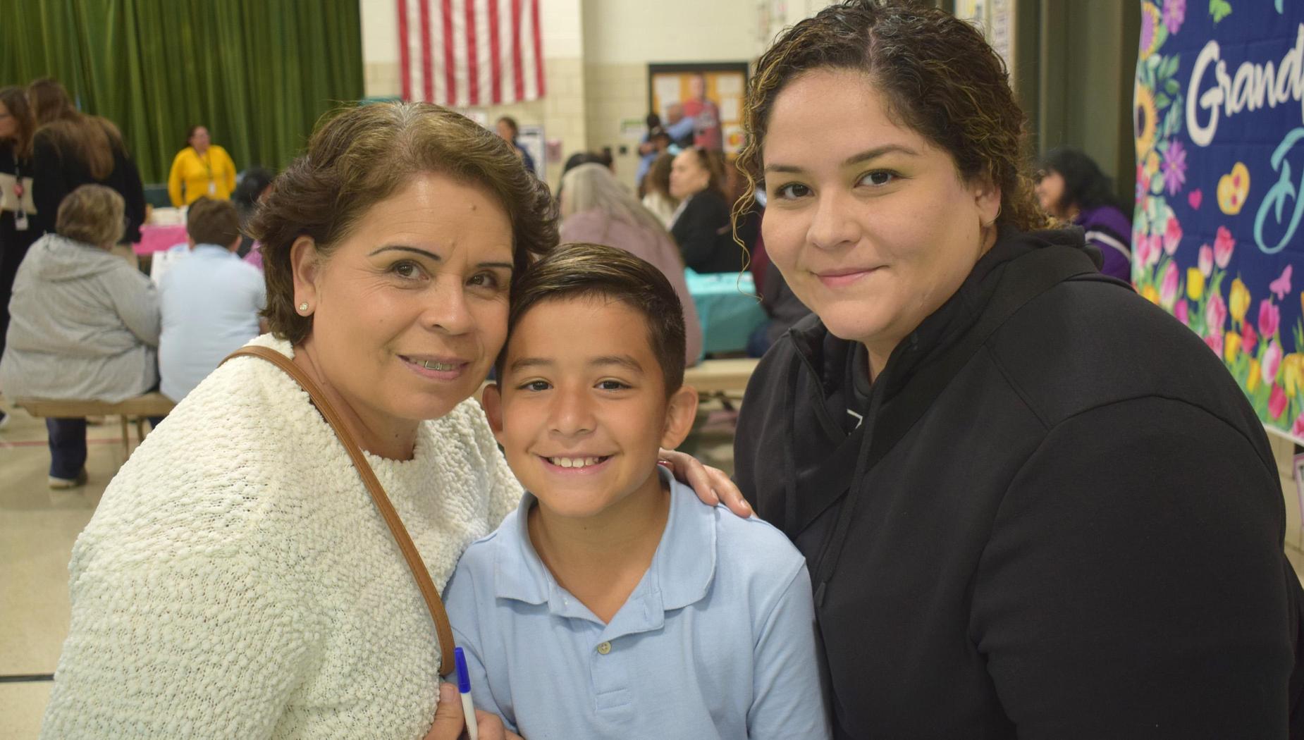 A woman, a young boy, and another woman smiling together in a school setting.
