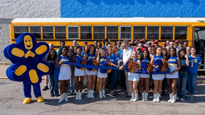 Two people cutting a ribbon in a crowd in front of a school bus