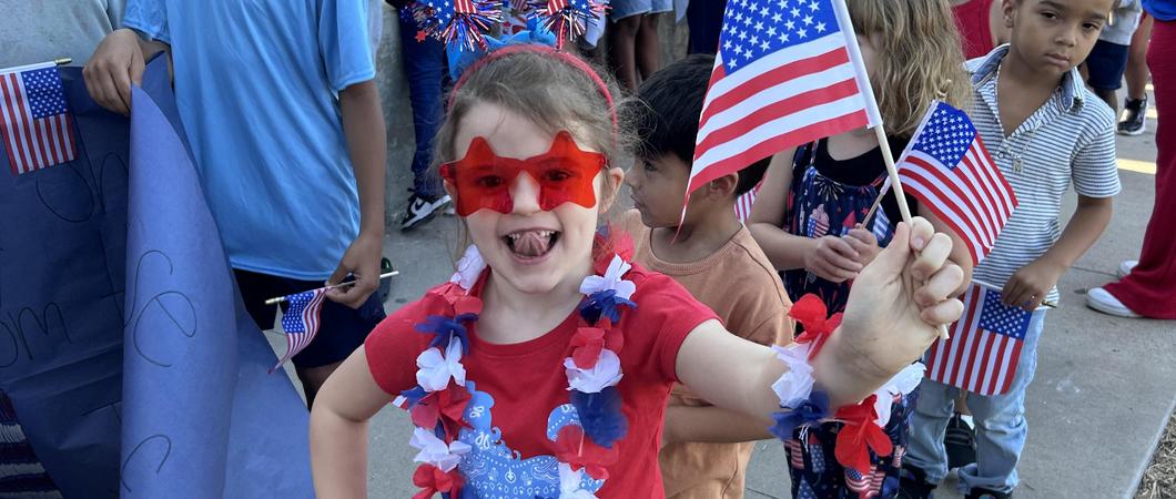 A child dressed in red white and blue, holding an American flag.