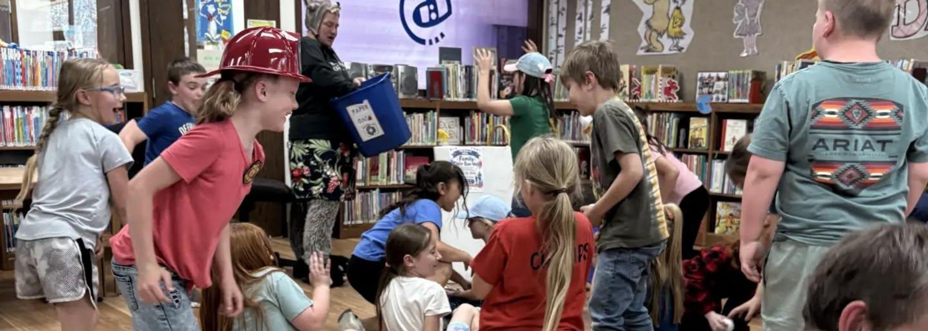 Children playing and interacting in a library setting with books around.