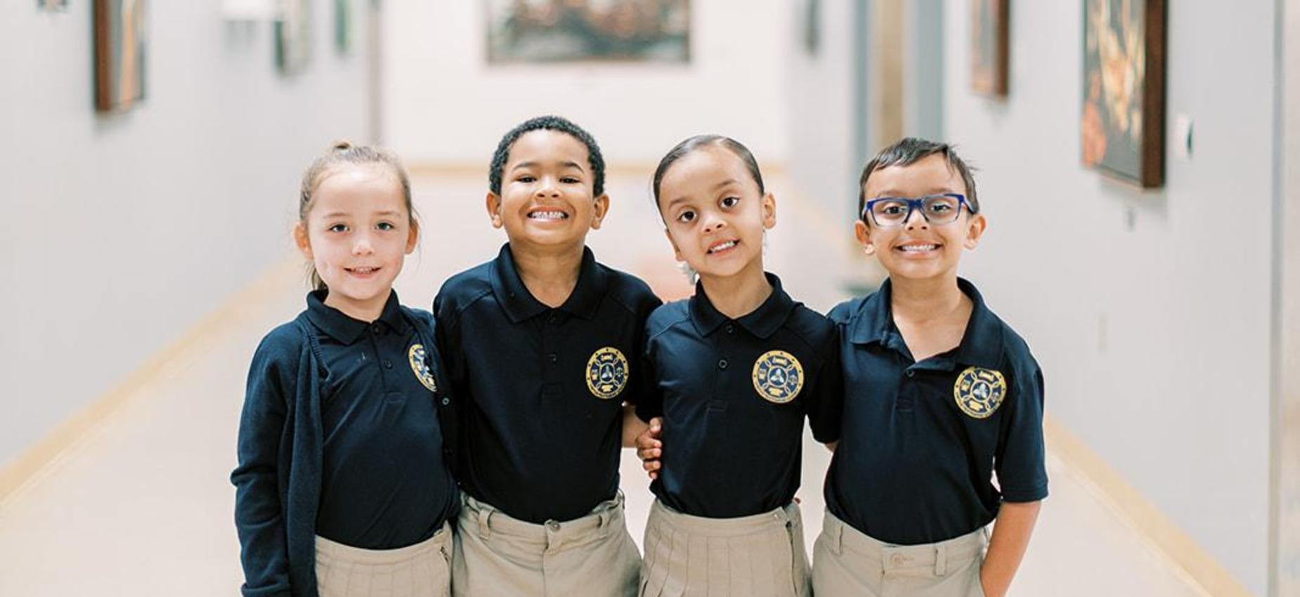 Four smiling elementary students stand together in a school hallway
